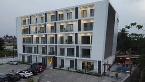 A multi-story hotel with a modern design, featuring balconies on each floor, a parking area with several cars, and a pool area visible in the background. - Oasis Retreat at 233 Boulevard (Accra)