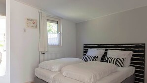 A bedroom with a bed, a window with curtains, a radiator, and a wall-mounted picture. - Beach House in Callantsoog near Scenic Beach (Callantsoog)