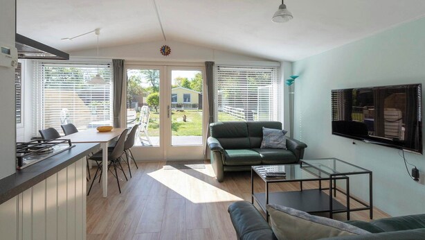 A modern living room with a sofa, a glass coffee table, and a TV mounted on the wall. - Beach House in Callantsoog near Scenic Beach (Callantsoog)
