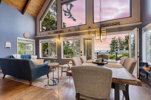 A spacious living area with a high ceiling, large windows, and a view of the outdoors.