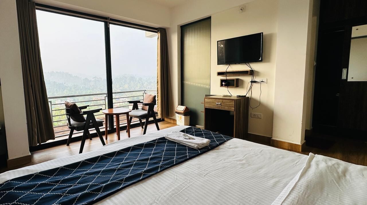 Habitación de hotel con una cama grande, un escritorio, una silla, un televisor y un balcón con vistas.
