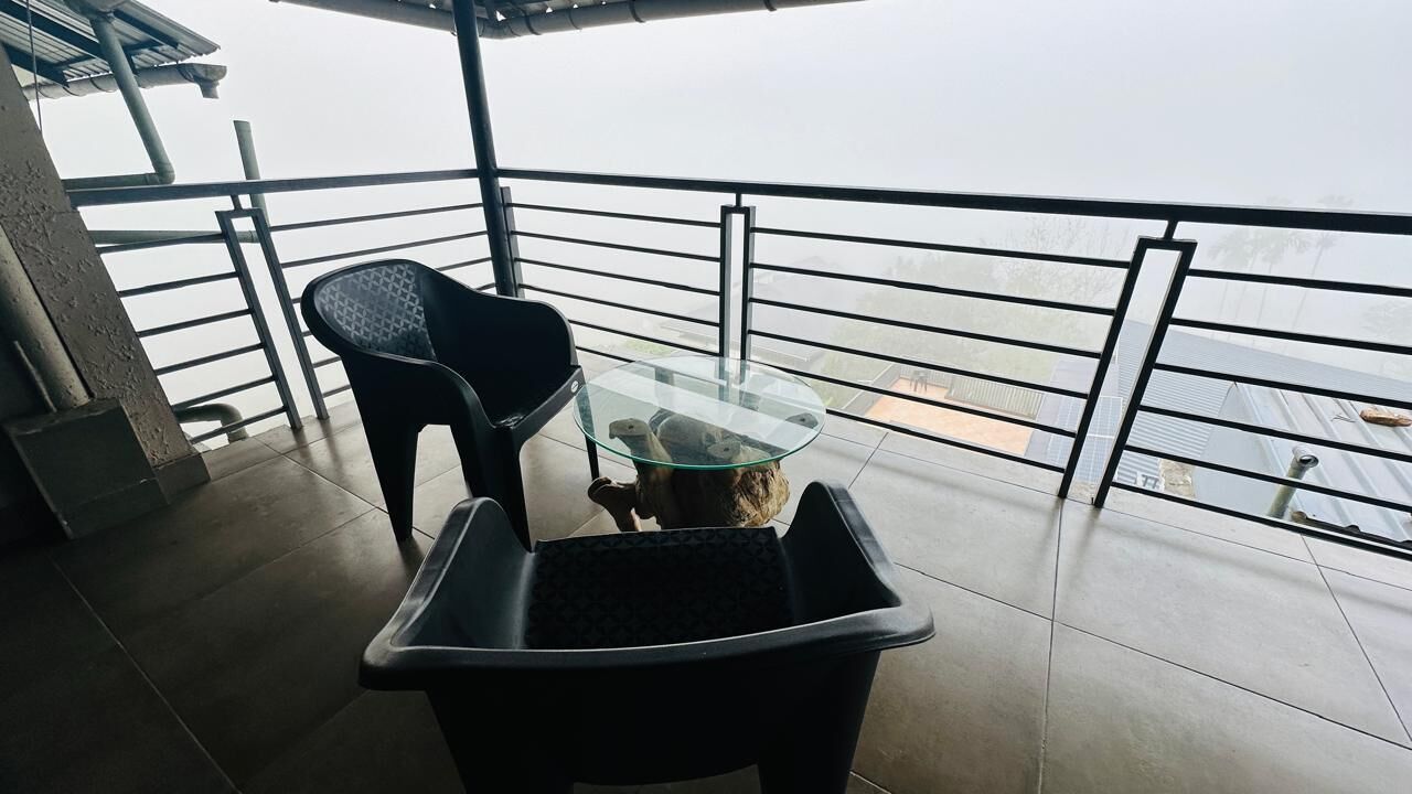 A balcony with a glass table, a chair, and a trash bin.