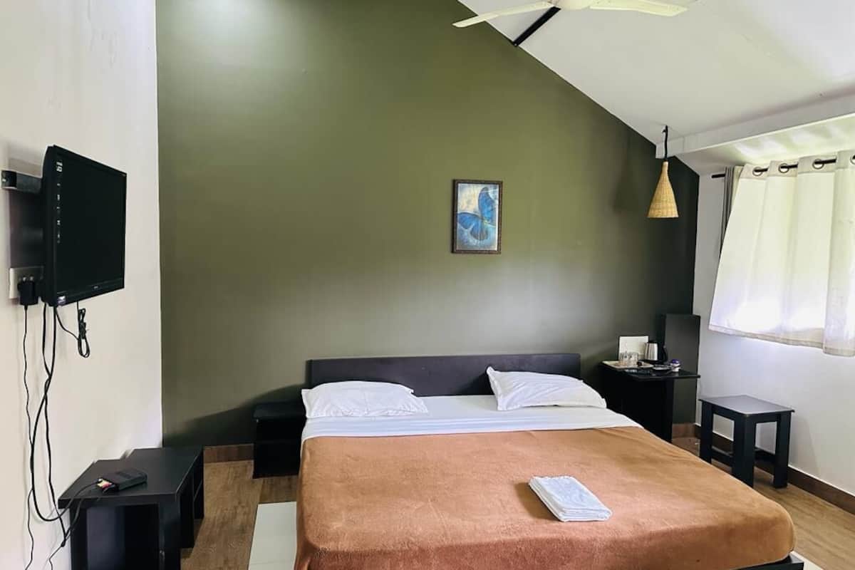 Un dormitorio con cama, televisor de pantalla plana montado en la pared, ventilador de techo, mesita de noche y tocador.