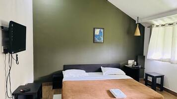 A bedroom with a bed, a flat-screen TV mounted on the wall, a ceiling fan, a bedside table, and a nightstand.
