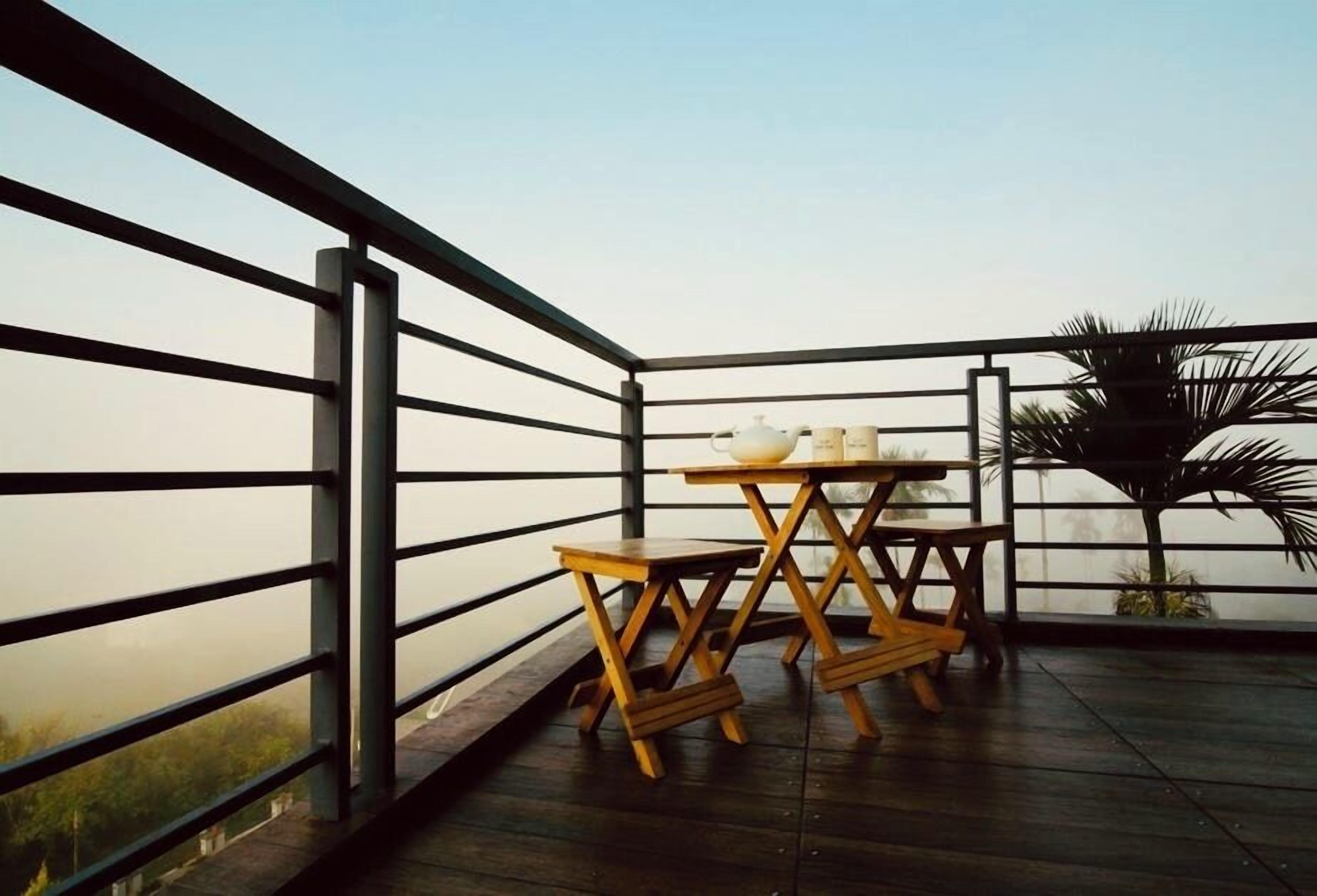 Een balkon met een houten tafel en stoelen, een hekwerk en uitzicht op zee.