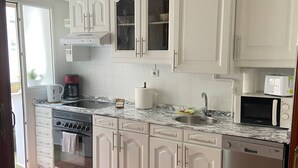 Una cocina con armarios blancos, encimera de mármol, lavavajillas, estufa, microondas y fregadero.