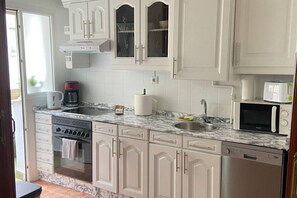Cucina con mobili bianchi, un piano di lavoro in marmo, lavastoviglie, fornello, forno a microonde e lavello.