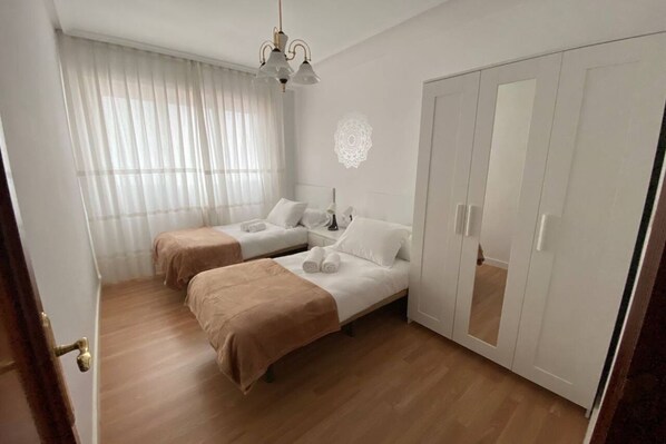 A hotel room with two beds, a wardrobe, a mirror, and a chandelier.