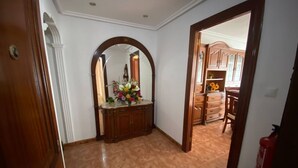 Un pasillo con una puerta de madera, un espejo y un arreglo floral sobre un mueble.