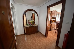 Un corridoio con una porta in legno, uno specchio e un vaso di fiori su un mobiletto.