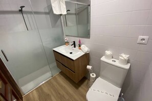 Un bagno moderno con cabina doccia in vetro, mobile bagno in legno, lavandino bianco, specchio e water.