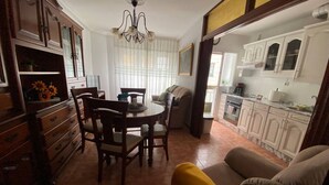 Un comedor con una mesa redonda y sillas, un sofá, y una cocina con armarios blancos.