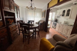 Zona pranzo con tavolo rotondo e sedie, divano e cucina con mobili bianchi.