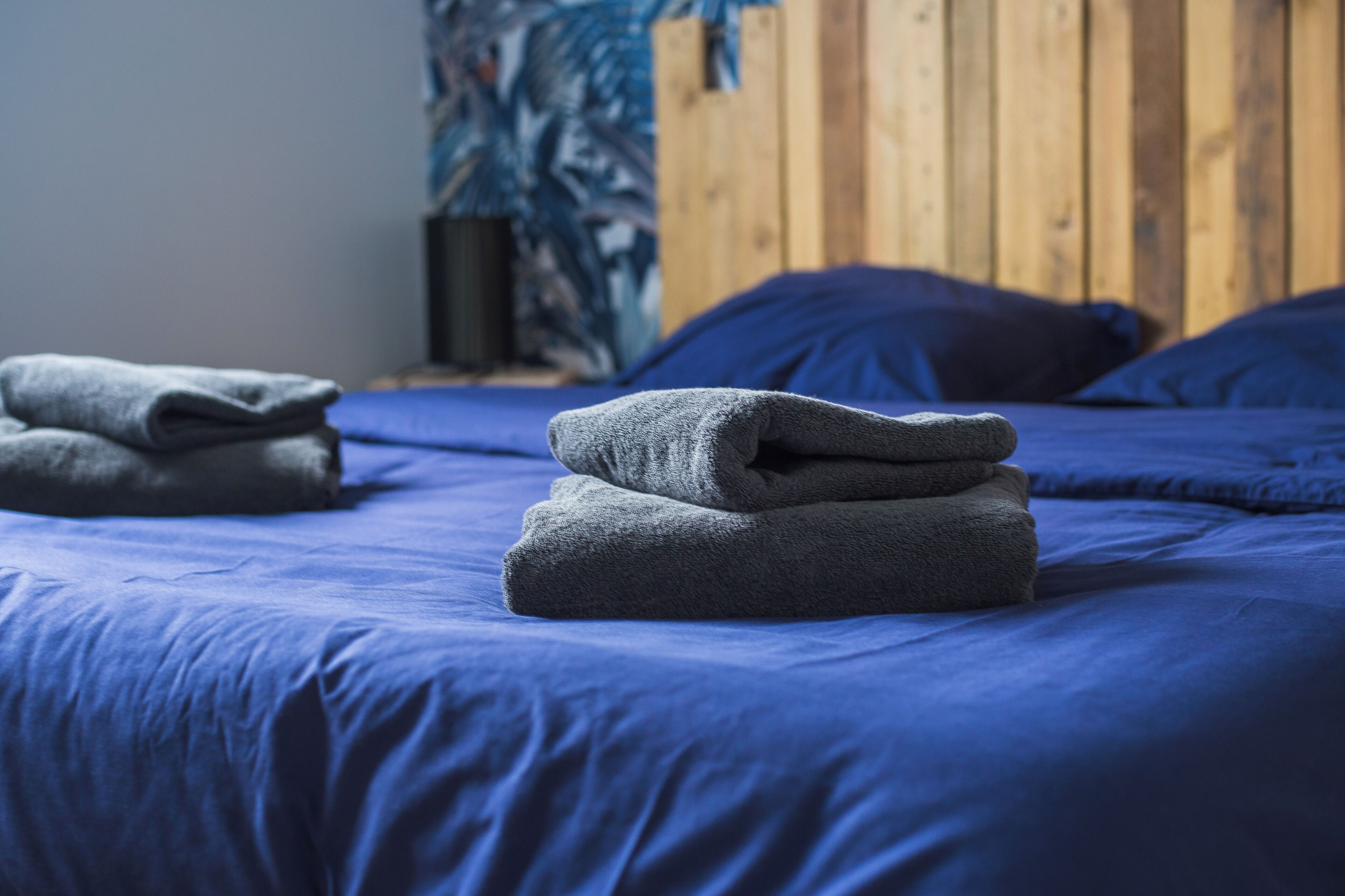 Una cama bien tendida con ropa de cama azul y toallas dobladas.