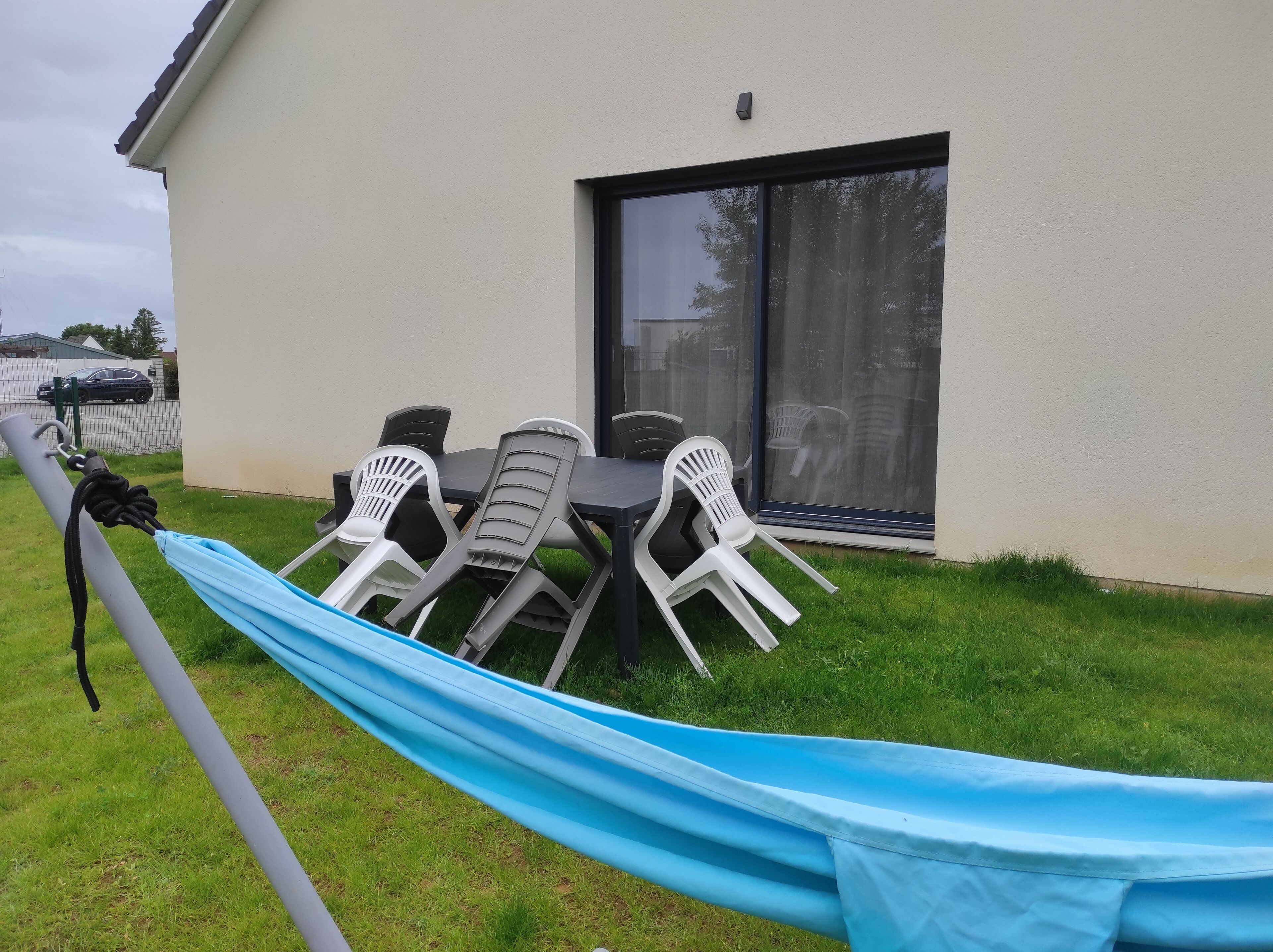 Une terrasse avec une table et des chaises, un toboggan bleu et un bâtiment doté d’une grande fenêtre.