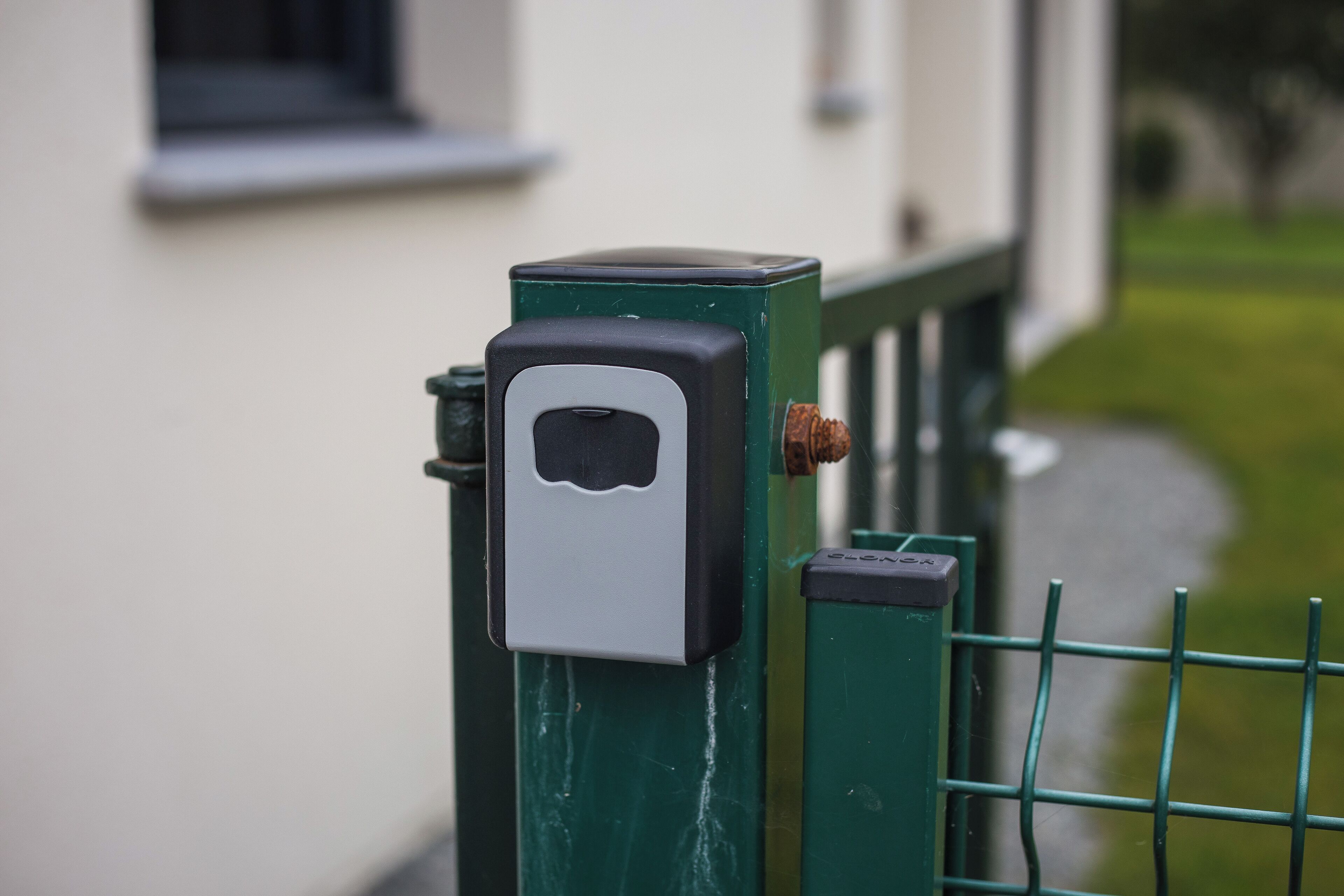 A green metal gate with a rectangular lockbox attached to it.