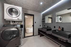 Enjoy a refreshing shower in the sleek bathroom with a wall-mounted washer and dryer, spacious sink area, and large mirror.