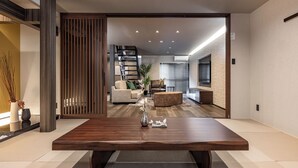 A modern living room with a wooden dining table, a sofa, and a staircase leading to another level. - JAPAVISTA Radiant (Osaka)