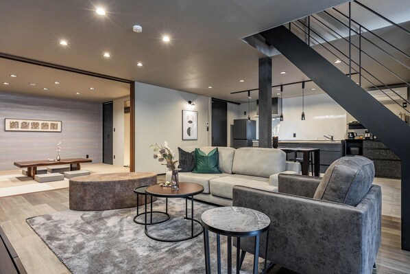 Relax in this stylish living space with a sofa, coffee table, and bench on a patterned rug. Enjoy meals at the dining table and kitchen area with a refrigerator and coffee machine.