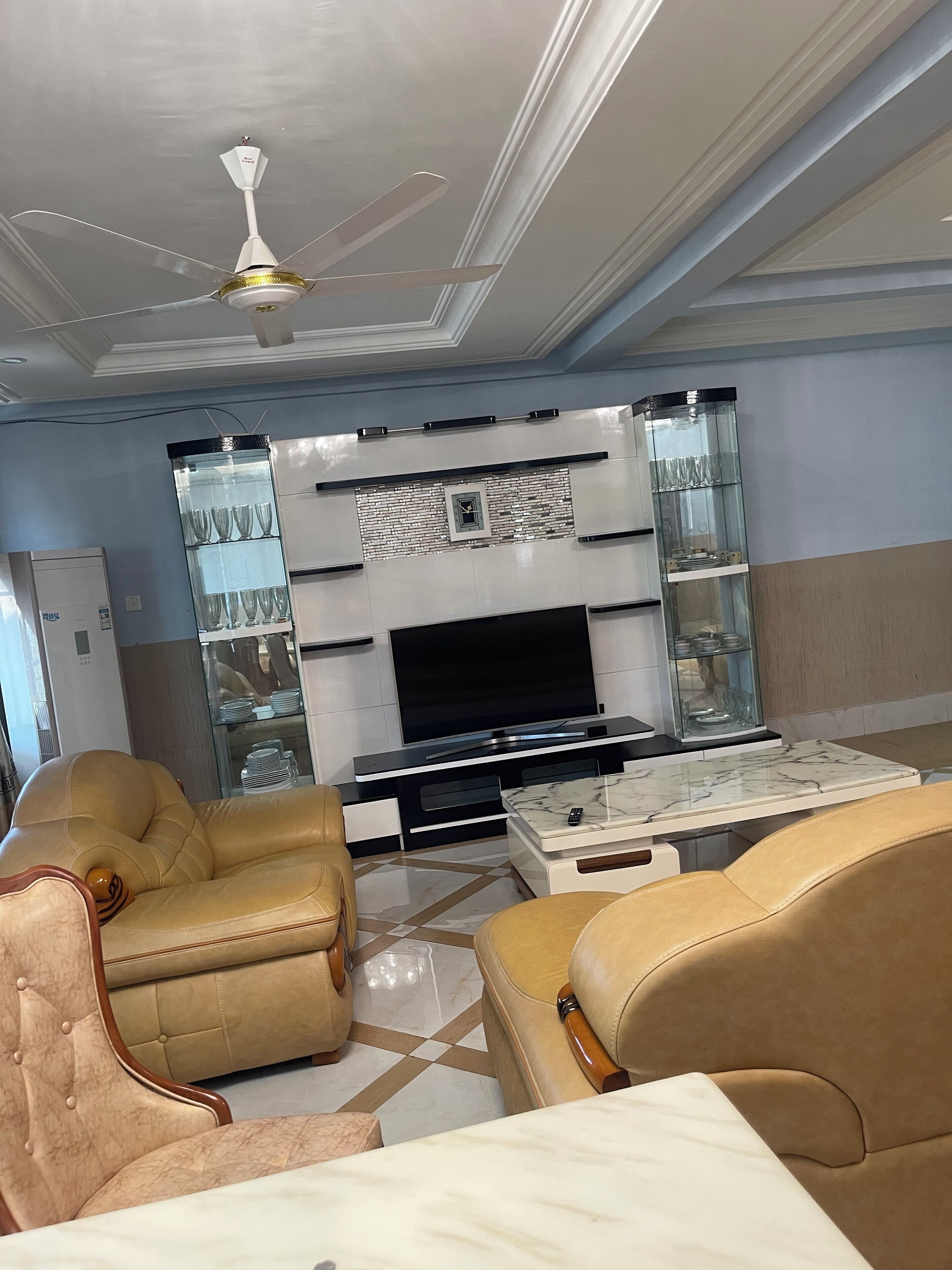 Una sala de estar moderna con televisor de pantalla plana, sofás de cuero, una mesa de centro de mármol y un aparador de vidrio.