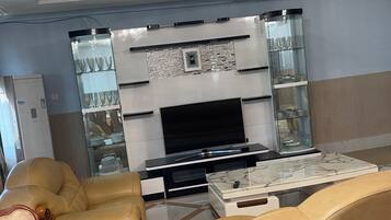 Una sala de estar moderna con televisor de pantalla plana, sofás de cuero, una mesa de centro de mármol y un aparador de vidrio.