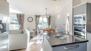 A modern kitchen with a built-in oven, a dining area with a table and chairs, a sofa, and a large window with curtains.