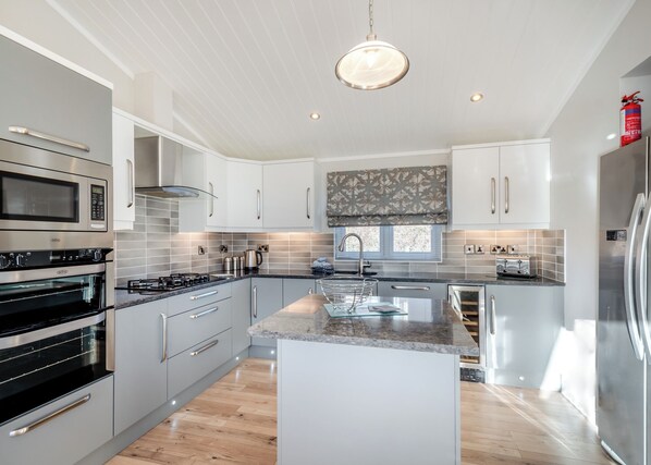 A modern kitchen with stainless steel appliances, white cabinetry, a central island, and a large window.