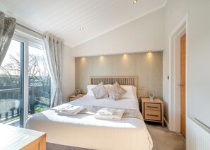 Ein Schlafzimmer mit einem großen Bett, zwei Nachttischen, einem Fenster mit Vorhängen und Blick ins Freie.
