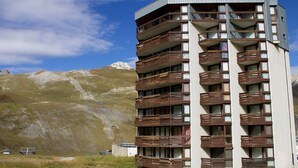 Un immeuble à plusieurs étages, doté de balcons, qui se dresse sur un fond de paysage montagneux.