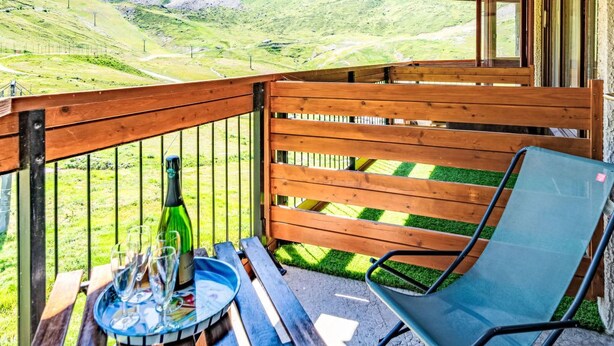 Une terrasse en bois avec une table et des chaises, offrant une vue sur un paysage montagneux.