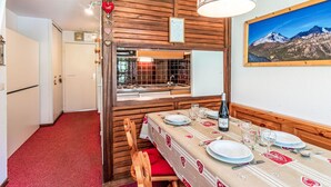 Un coin repas avec une table dressée pour deux personnes, une bouteille de vin et un tableau représentant un paysage de montagne accroché au mur.