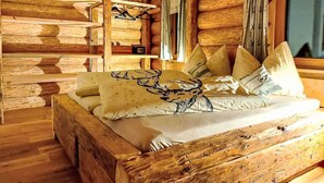 Una camera in legno tipica di una baita, con un letto decorato con un cuscino a tema cervo, pareti in legno e una finestra con tende.