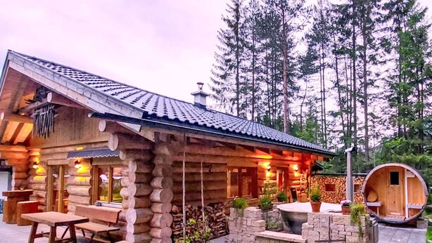 Un rustico chalet in legno con patio in pietra, panchine in legno e un piccolo giardino.