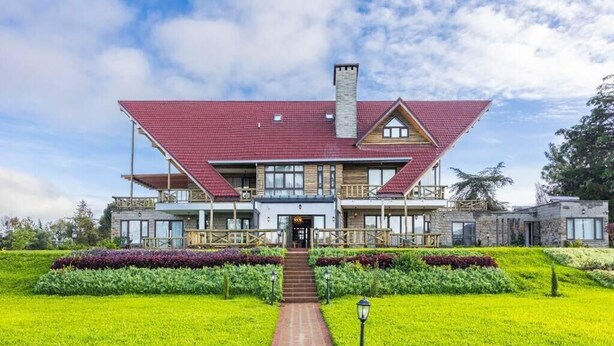 A large, two-story building with a red-tiled roof, a central entrance, and a well-maintained garden in front.