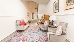 Un hall d’entrée spacieux, doté d’un tapis à motifs, de deux fauteuils, d’une petite table avec une lampe et d’un piano.
