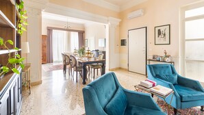 Un salon spacieux avec un coin repas, agrémenté d’un lustre, de fauteuils bleus et d’une grande fenêtre.