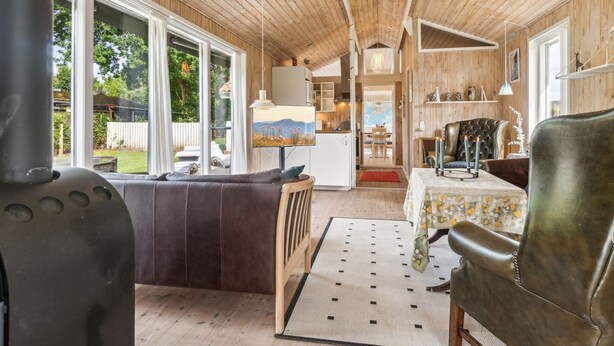 A cozy living room with a fireplace, a sofa, a dining table with chairs, and a view of the outdoors through large windows.