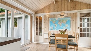 A wooden-paneled room with a dining table and chairs, a world map on the wall, and large windows.