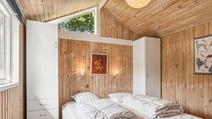 A bedroom with wooden walls, a bed with white bedding, a white wardrobe, and a painting on the wall.