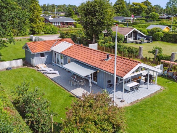 Uma casa com telhado de telhas vermelhas, varanda coberta com móveis de exterior e um gramado bem cuidado.