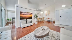 Een moderne woonkamer met een grote flatscreen-tv, een houten salontafel en een zithoek met een bank en fauteuils.