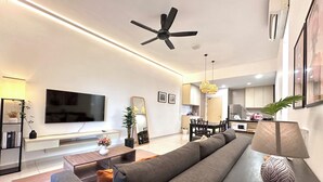 Una sala de estar moderna con un televisor de pantalla plana, un ventilador de techo y una zona de comedor con una mesa y sillas.