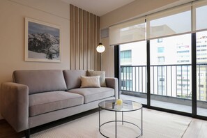 A modern living room with a grey sofa, a glass coffee table, and a large window with a view of buildings. - w* | Exceptional 2BR w/ Balcony in Miraflores (Miraflores)