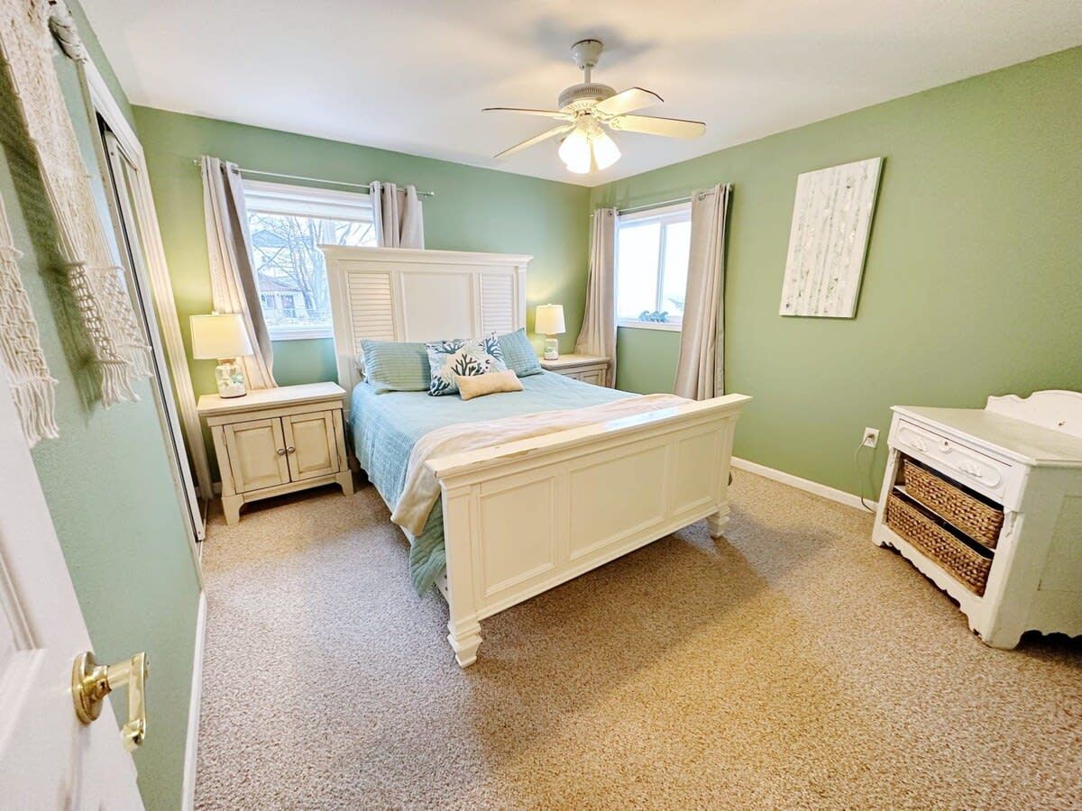 Une chambre à coucher comprenant un lit, des tables de chevet, une commode et un ventilateur de plafond.