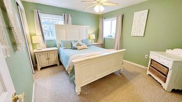 Une chambre à coucher comprenant un lit, des tables de chevet, une commode et un ventilateur de plafond.
