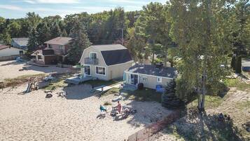A beachside property with a large house, a patio with outdoor furniture, and a sandy beach area.