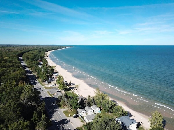 An aerial view of a coastal area with a beach, houses, and a road.