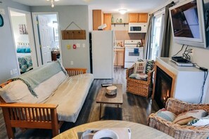 A compact living space with a sofa, a small table, a fireplace, a kitchen area with a microwave and stove, and a television.