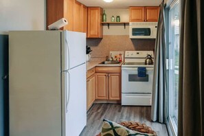 A compact kitchen with wooden cabinets, a white refrigerator, a microwave, and a stove.