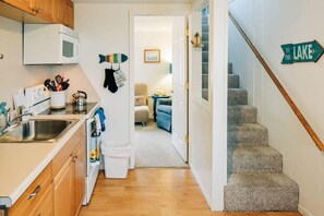A narrow hallway with a kitchen on the left, a staircase on the right, and a door leading to a living area.
